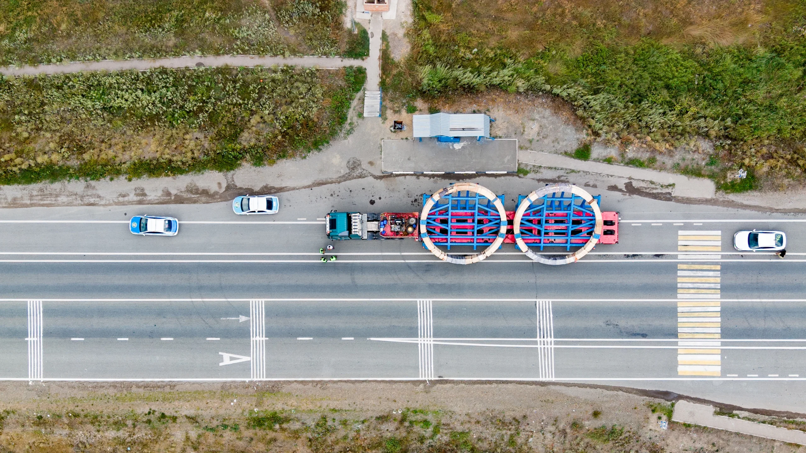 Yuqoridan ko'rinish: yirik gabaritli yuk tashish — patrul avtomobili kuzatuvida Volvo traktori modulli yarim tirkamada uzluksiz pressning ikkita yirik gabaritli sapfasi bilan